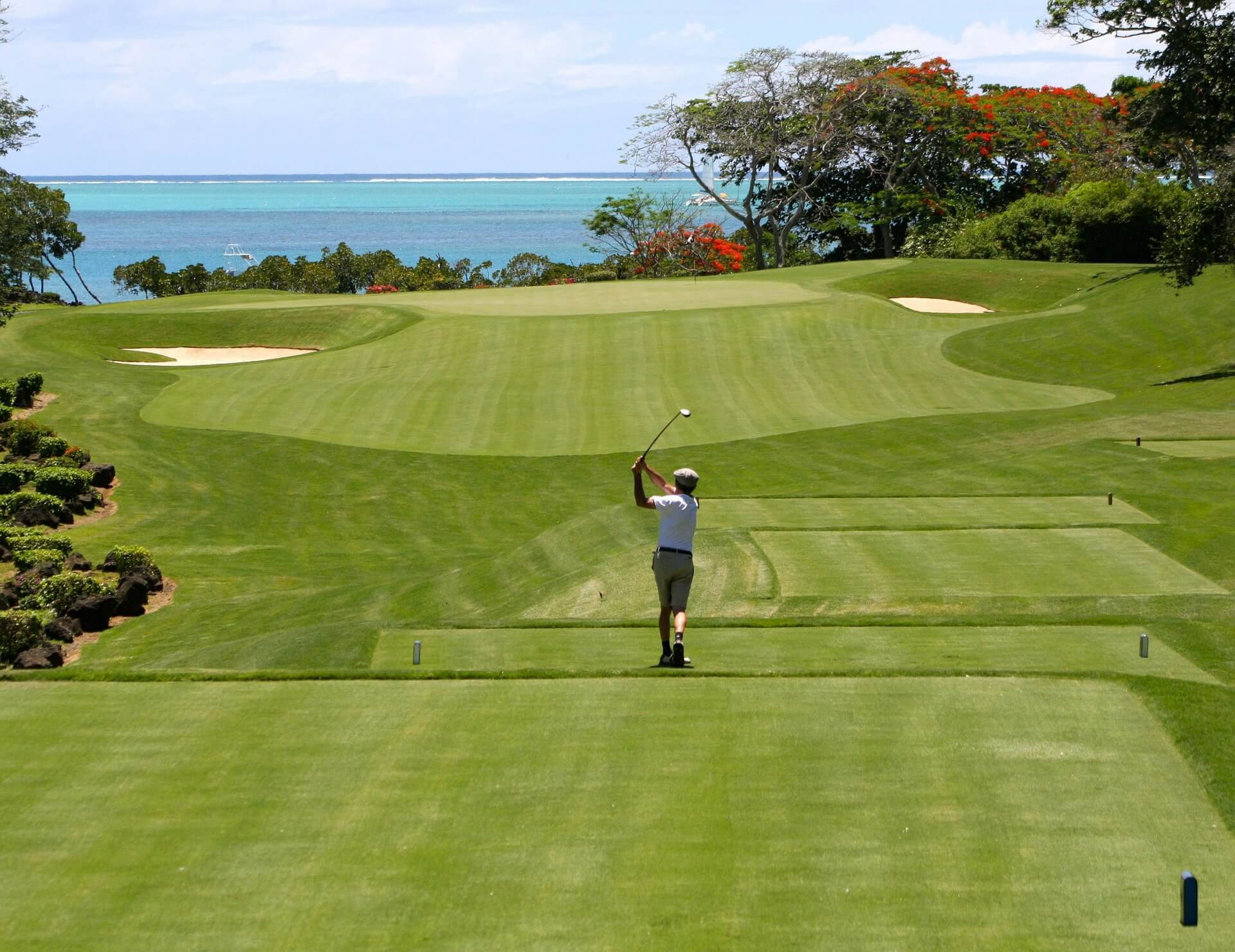 Far off shot of golfer taking a swing on the green with ocean in background