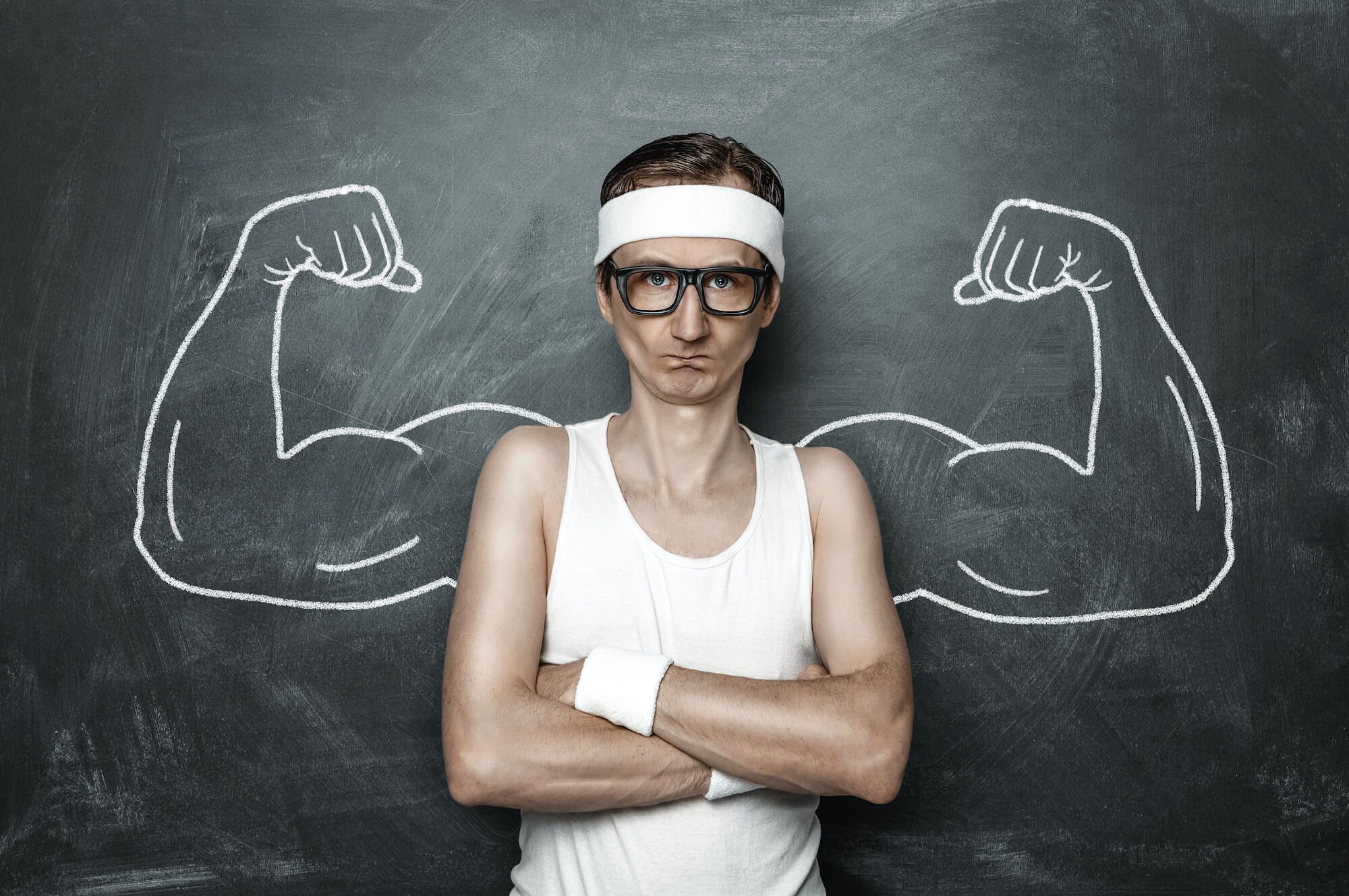 Skinny guys standing in front of chalk board with buff arms drawn on behind him