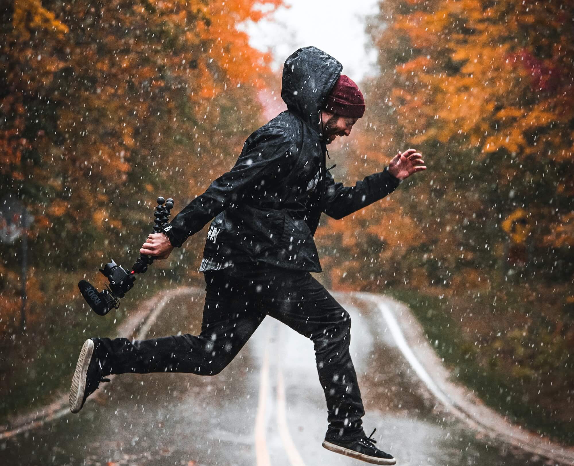 Man in jacket and toque running through rain with camera