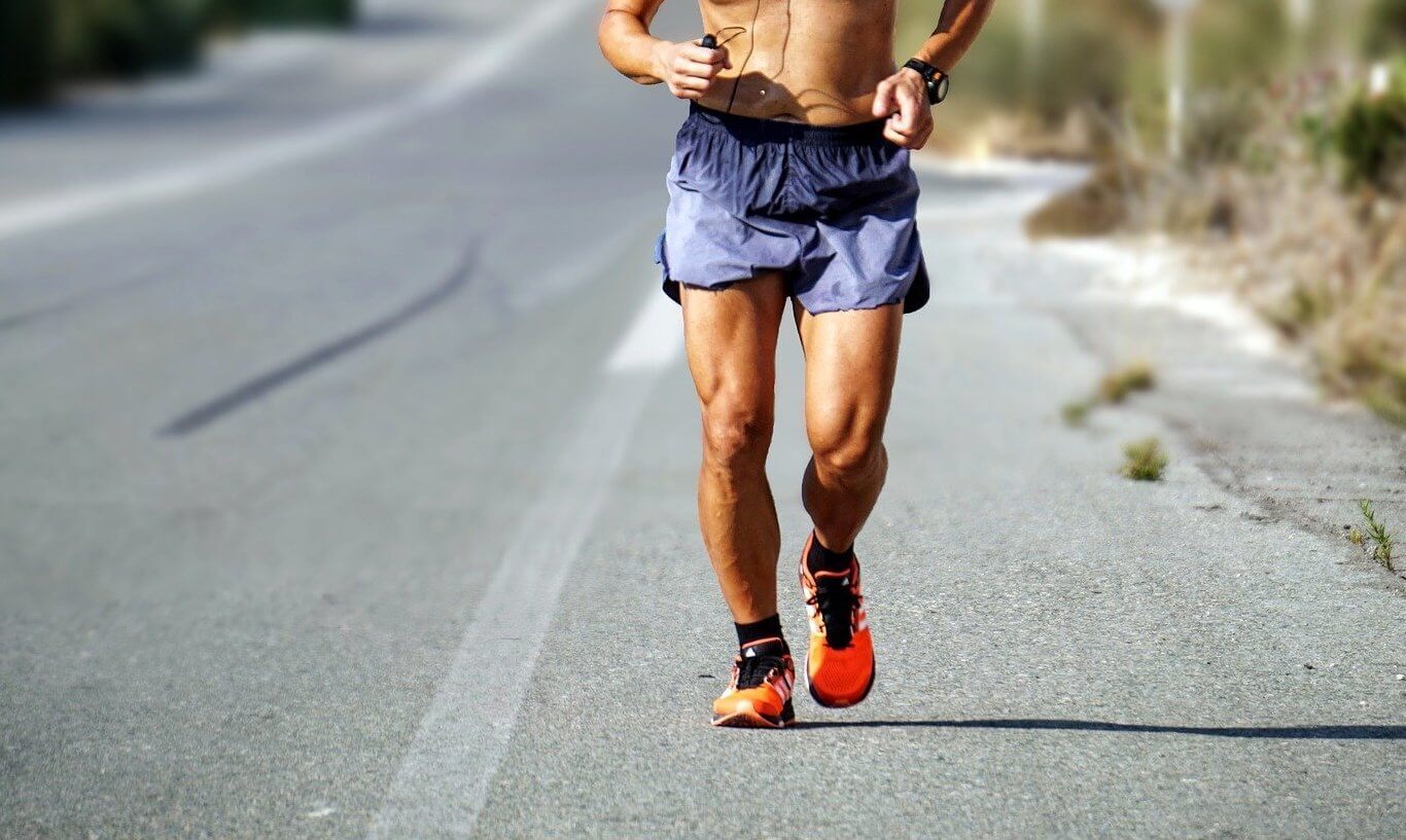 Shirtless man running on the street in shorts and sneakers