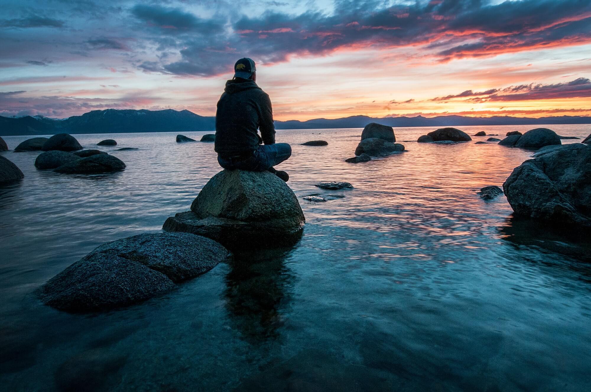 Man watching sunset sitting on rock surrounded by water