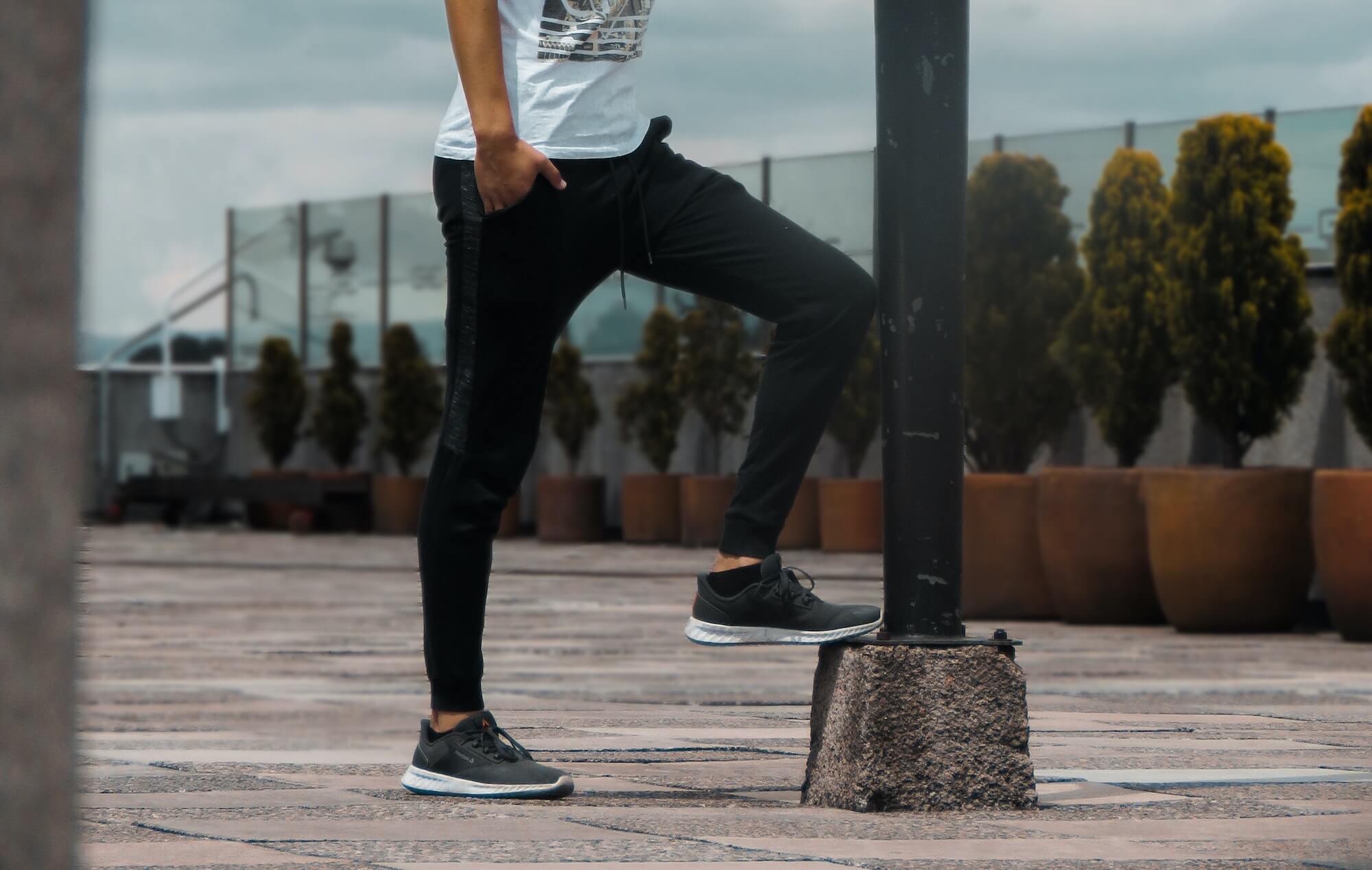 Man in black joggers and Reebok sneakers posing against lamp post