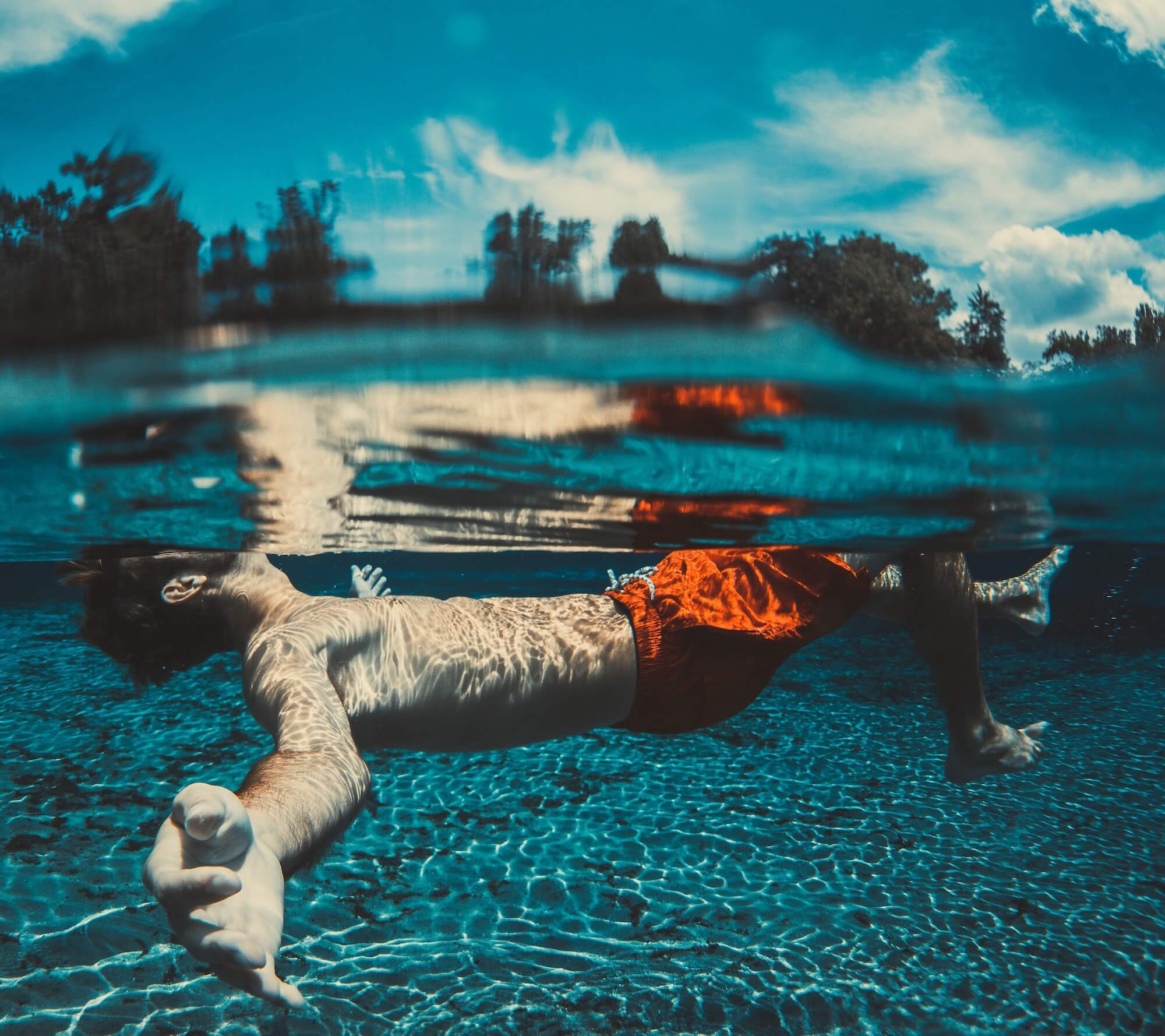 Man in orange swim trunks swimming in clear water