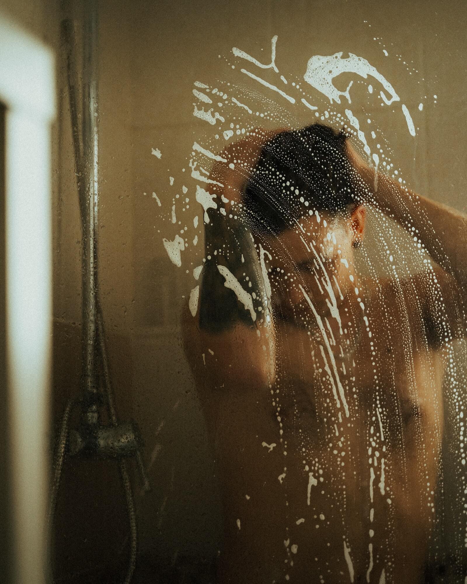 Man washing hair in shower with suds on the shower door
