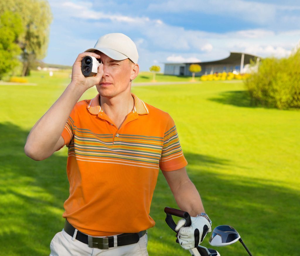 Man in orange golf shirt uses golf rangefinder on the course