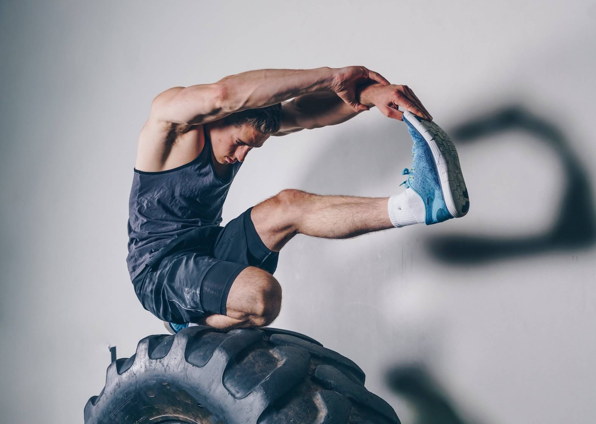 Man in fitness clothing stretching atop a large tire