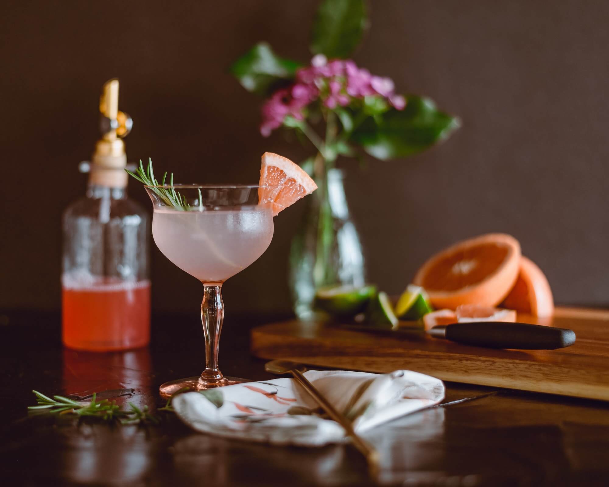 Pink cocktail in stemware with rosemary and grapefruit garnish