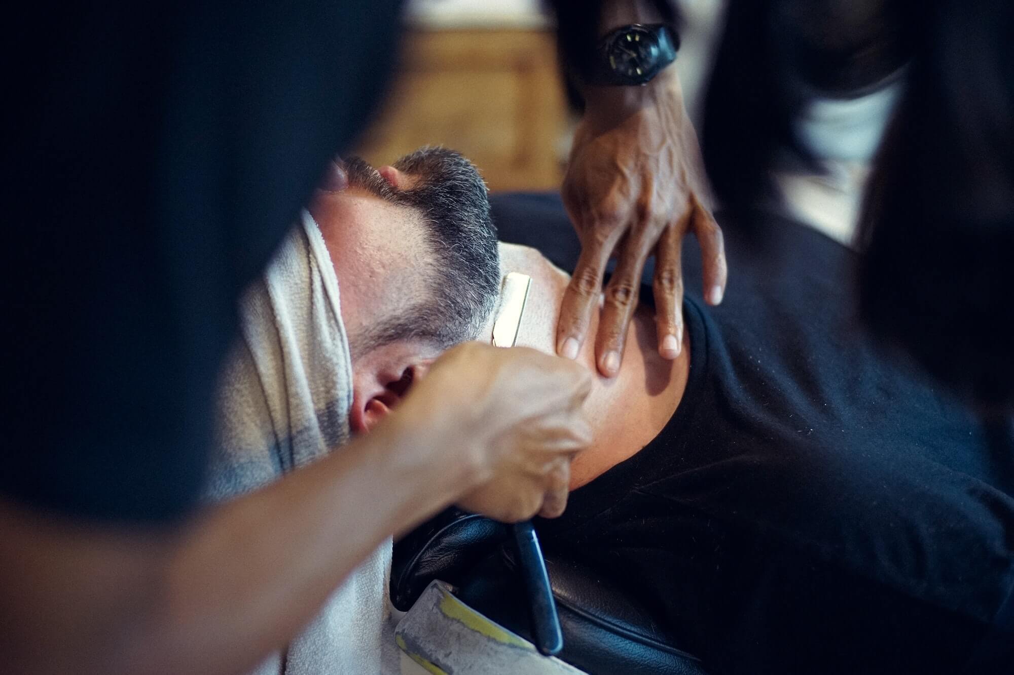 Man with beard receiving barbershop shave with straight razor