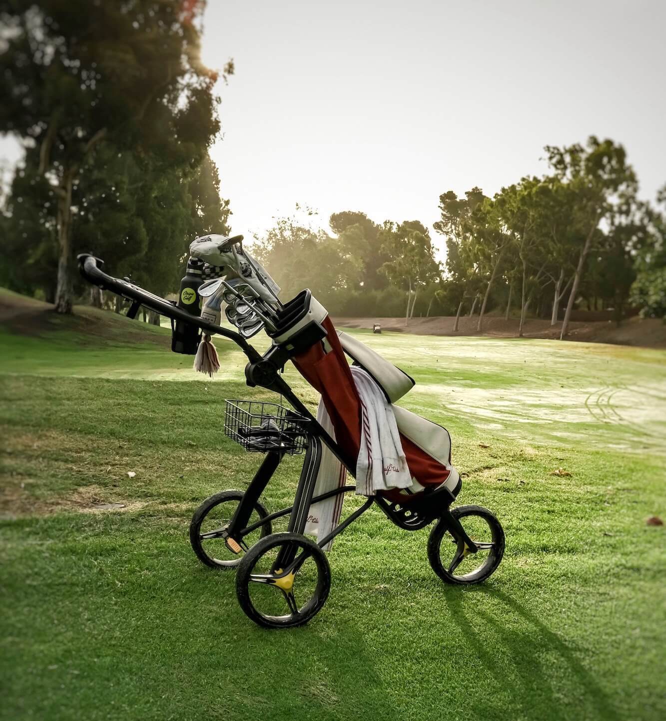 Golf push cart with golf bag sits on a green golf course