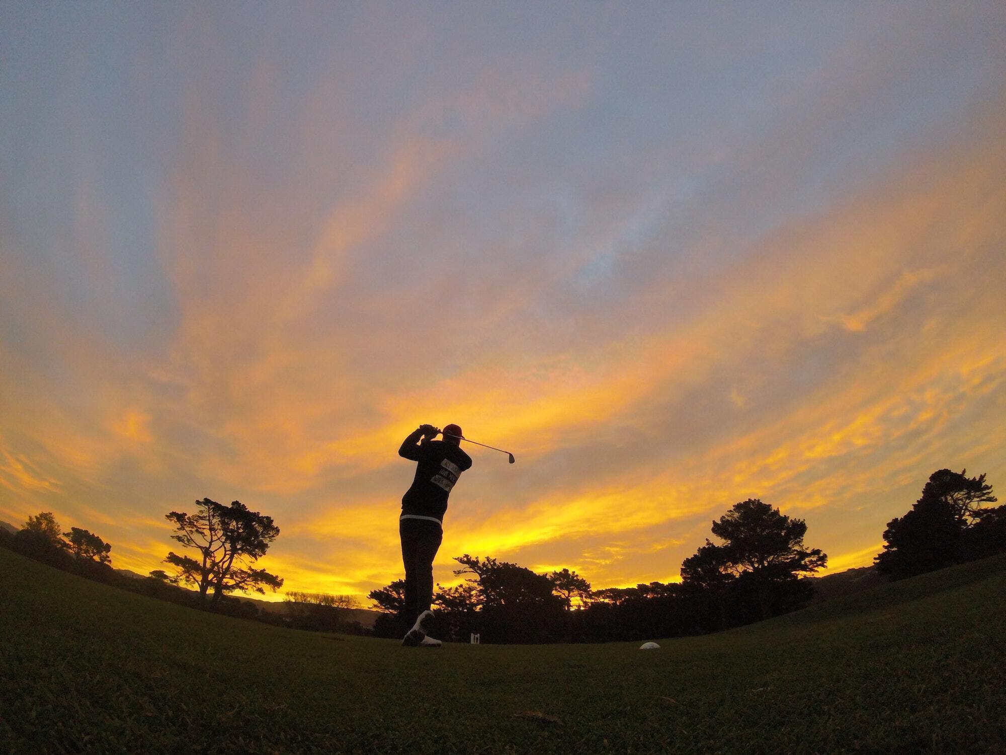 Man taking a swing on a golf course at sunset