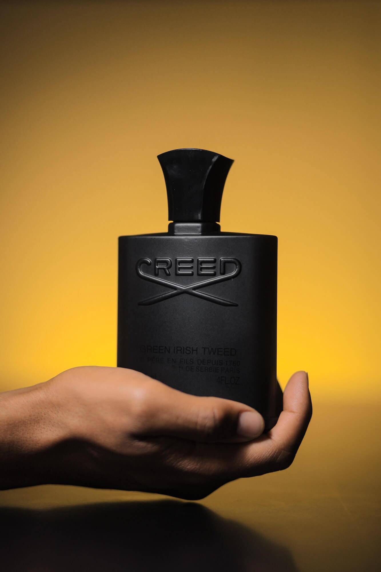 Man's hand holding bottle of Creed Green Irish Tweed cologne with yellow background