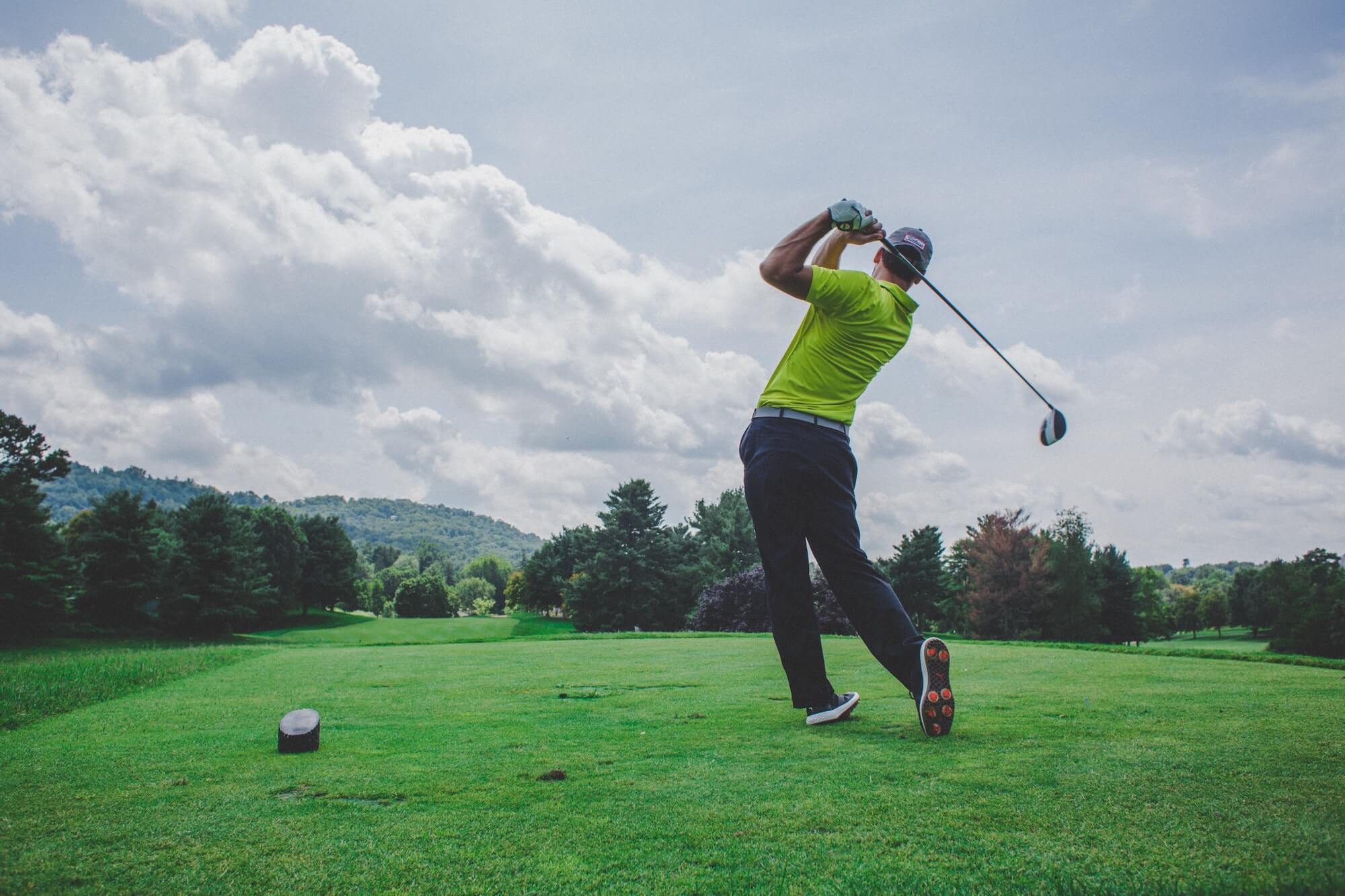 Man in lime green golf shirt, dark golf pants, and golf gloves swings golf club