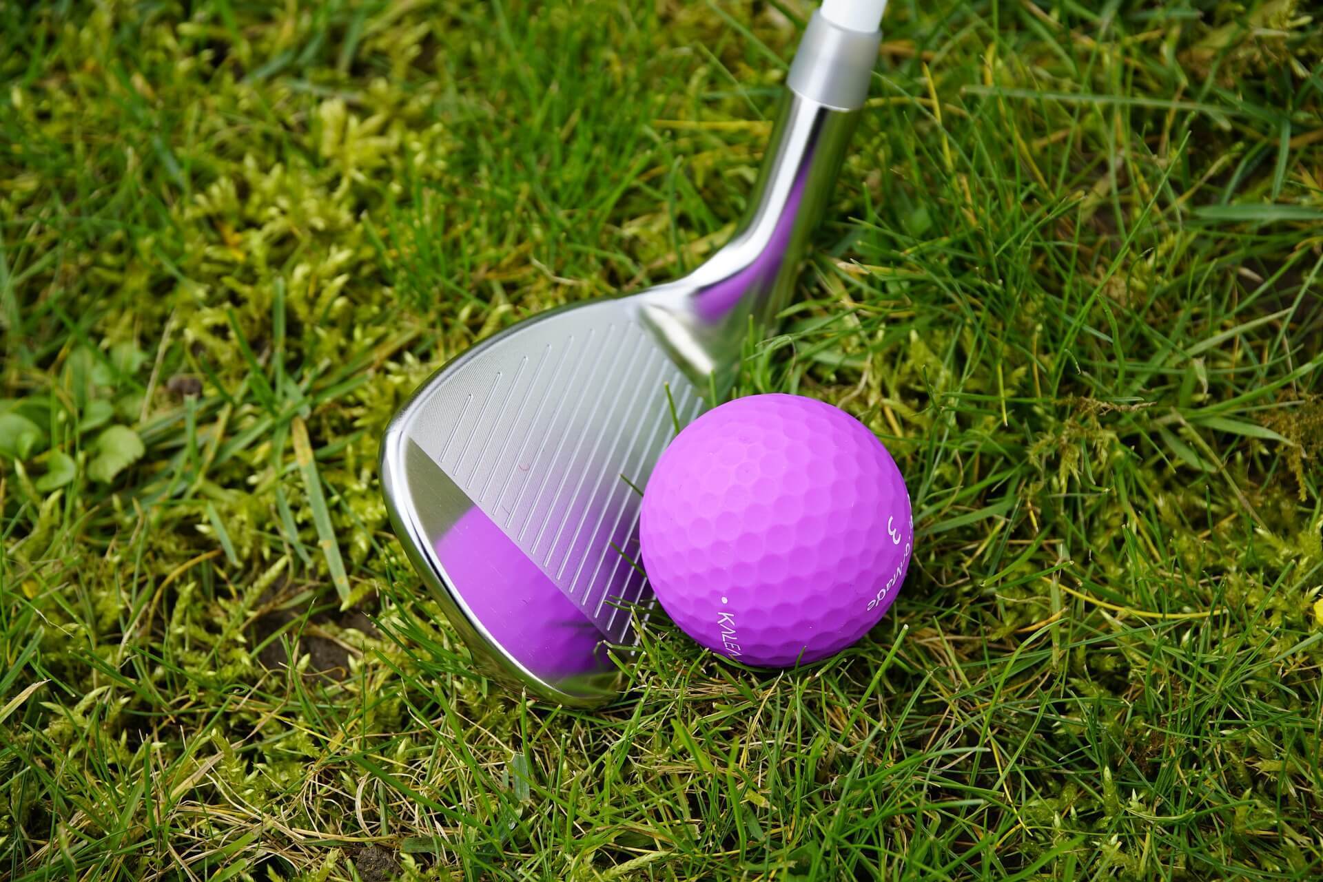 Close-up of golf wedge next to purple golf ball