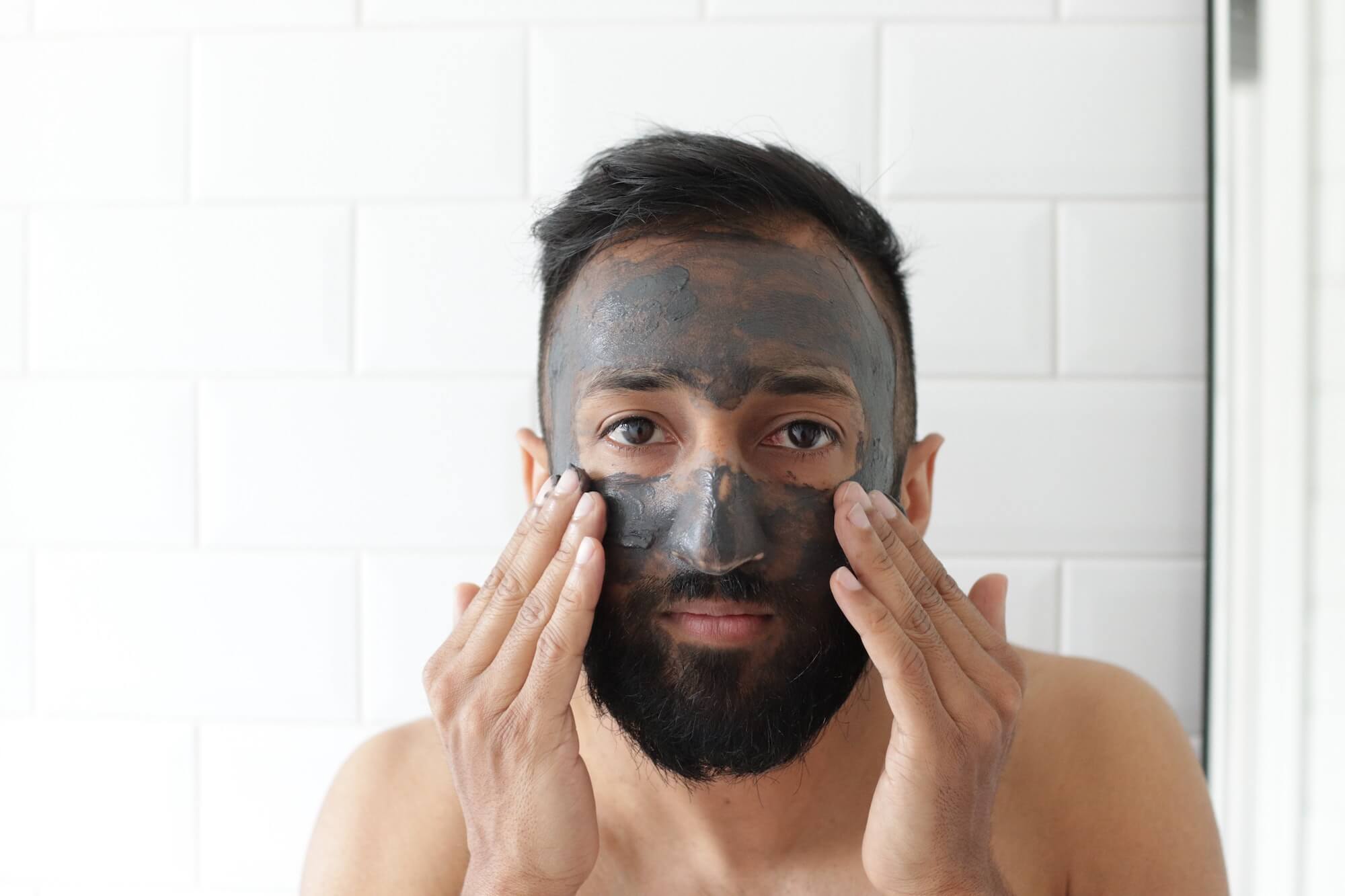 Man applying skin nourishing face mask in bathroom mirror