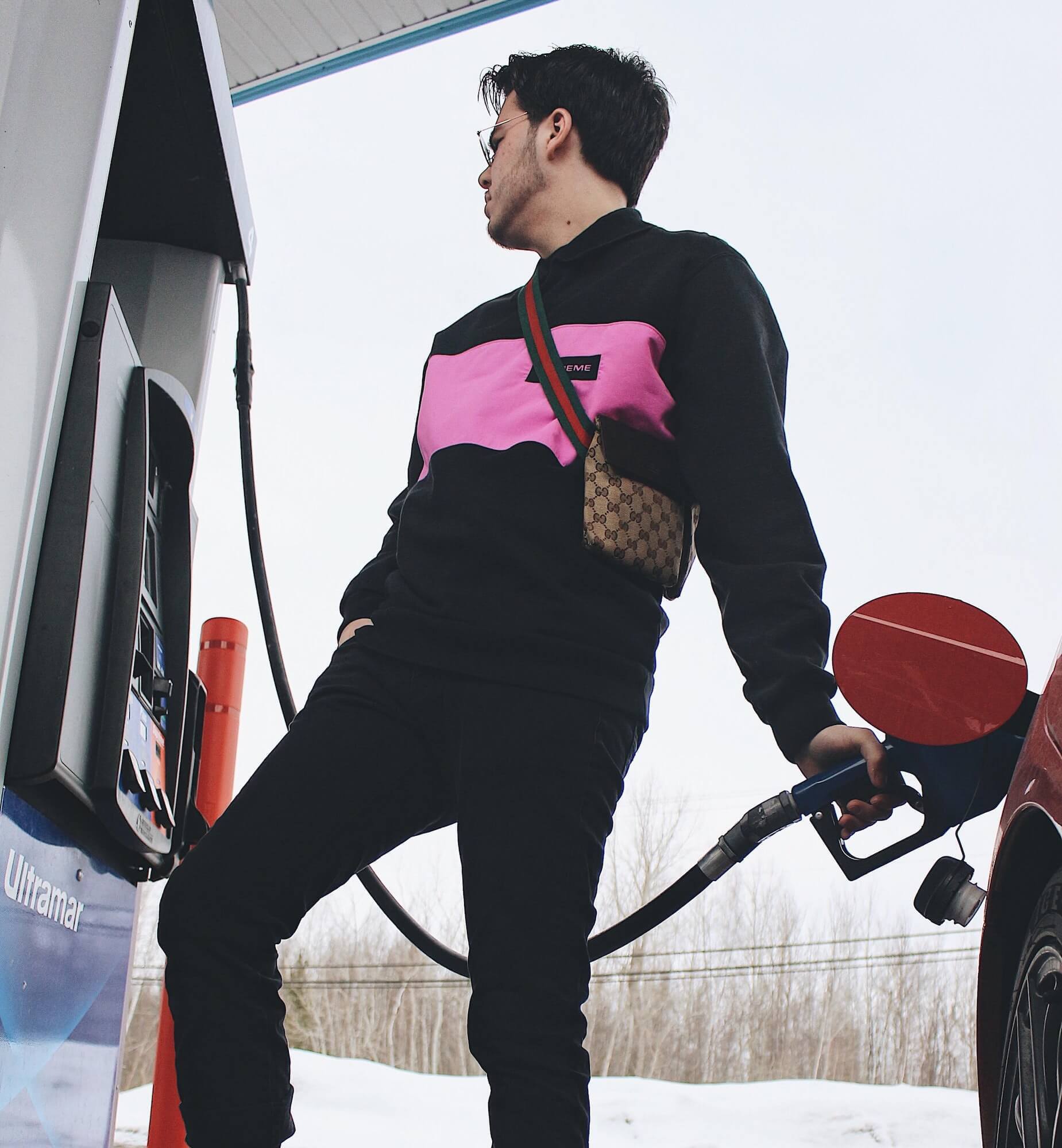 Man pumps gas wearing a Gucci crossbody bag