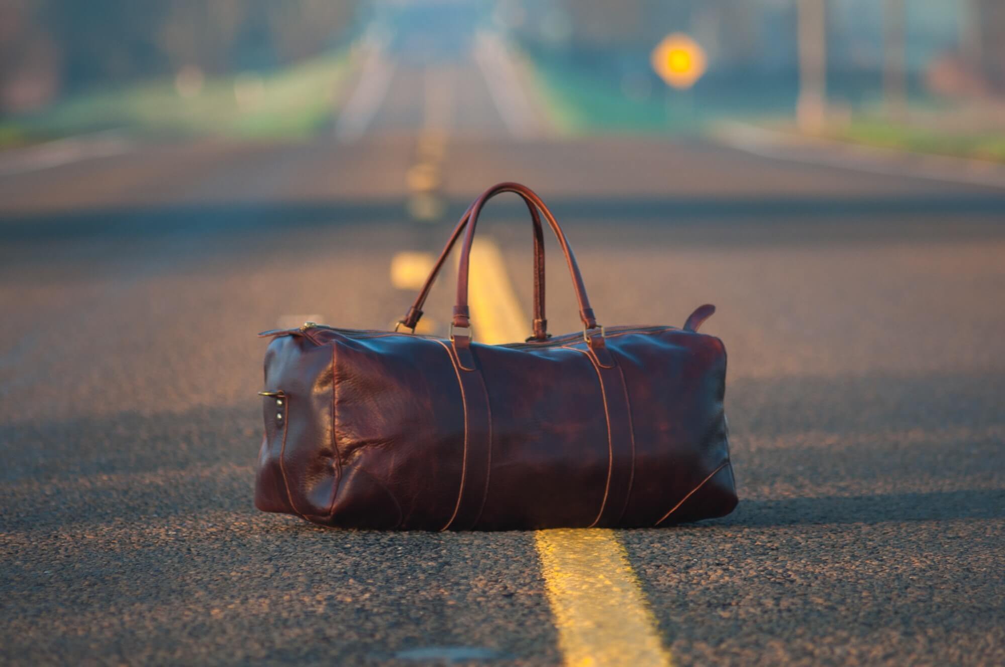 Brown leather duffle bag sits on the yellow line in the middle of an empty road