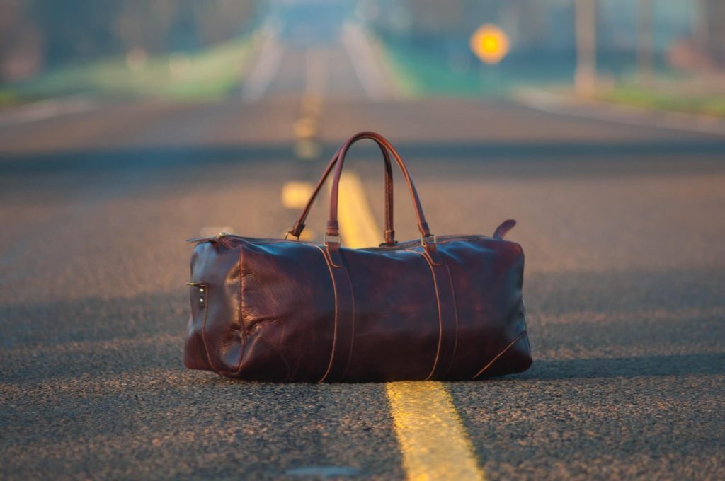 Brown leather duffle bag sits on the yellow line in the middle of an empty road