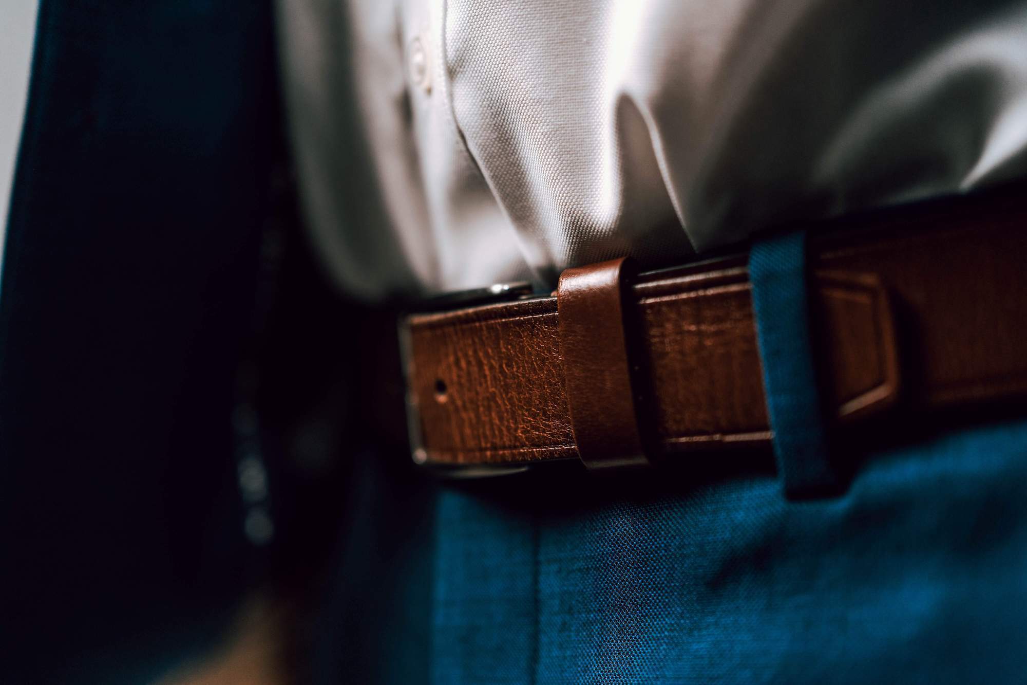 Close-up shot of man wearing blue dress pants with a brown leather belt