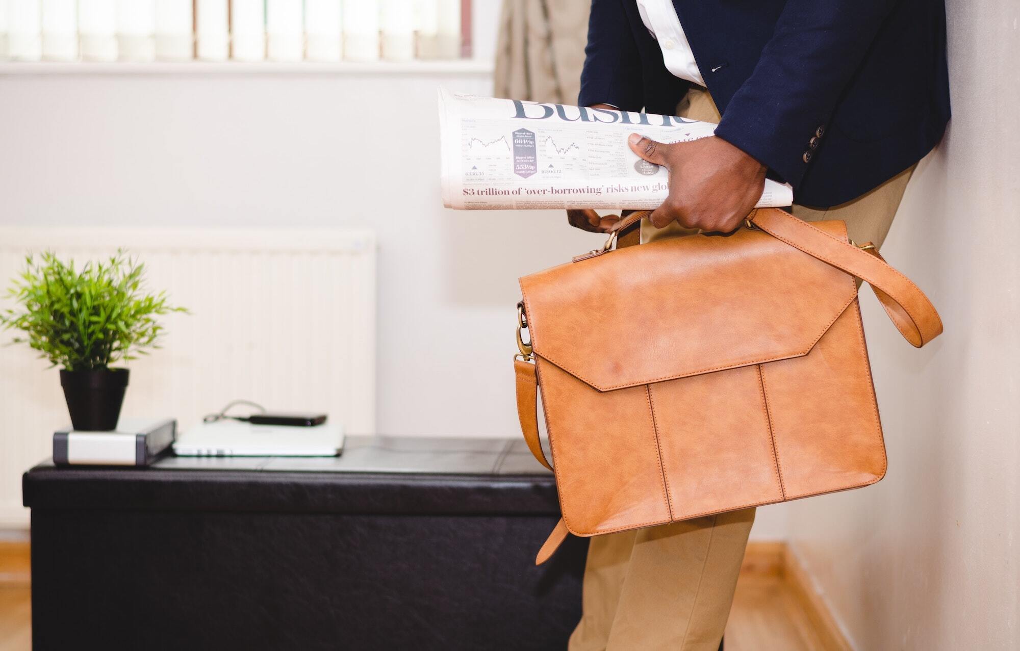 Man with newspaper carries men's leather work bag