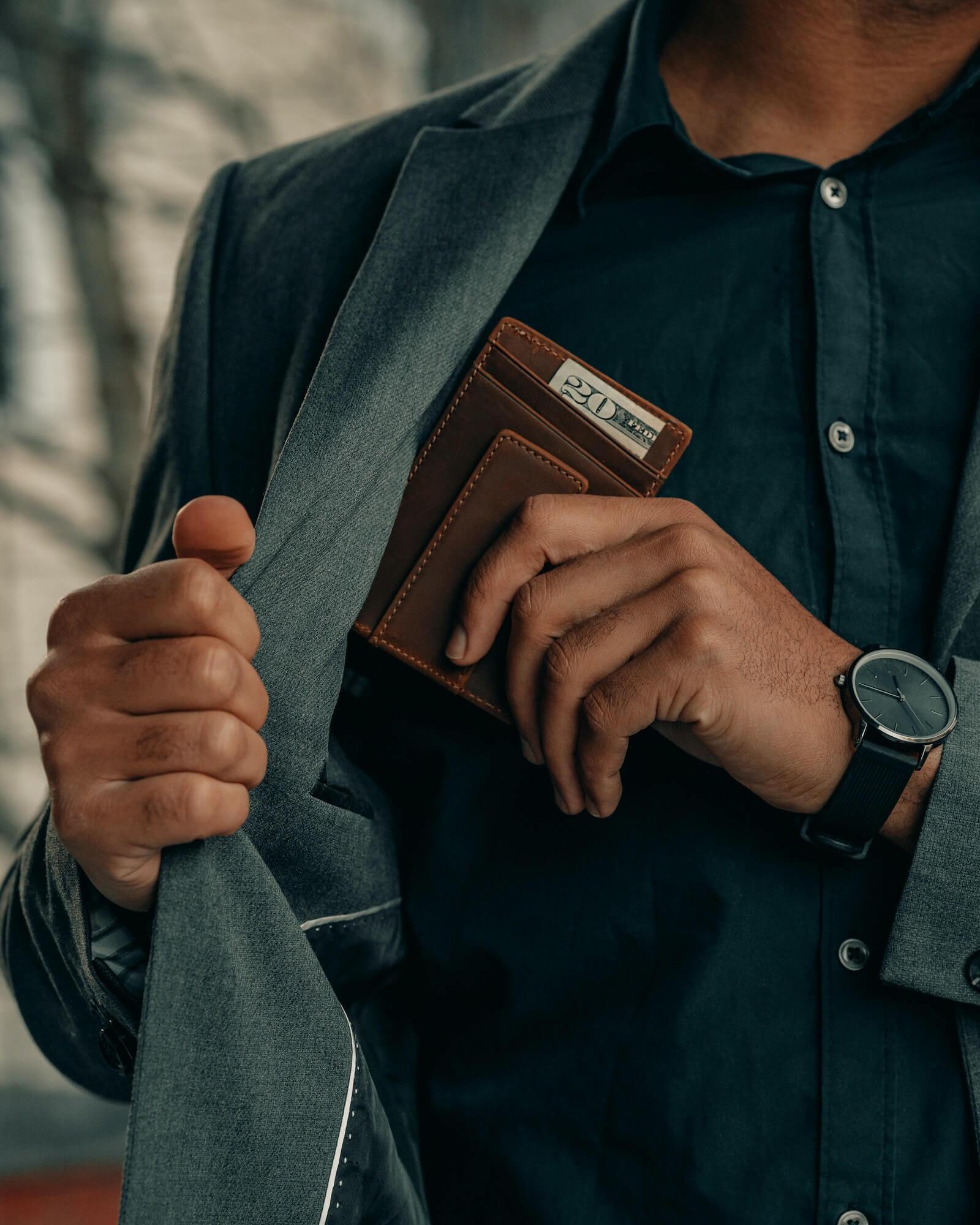 Man with blazer and wristwatch taking leather wallet from inside breast pocket